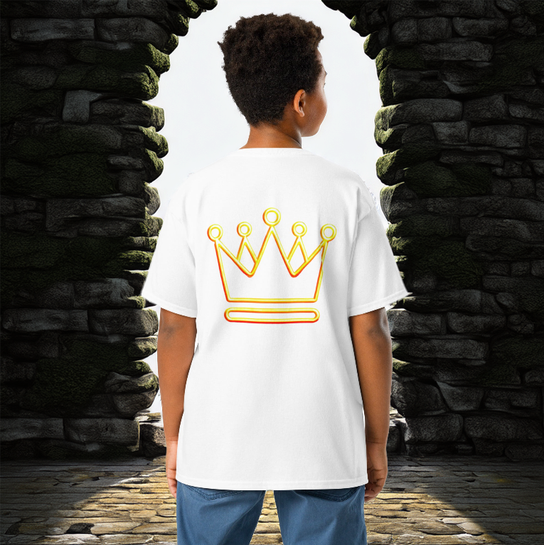 A young boy wearing a white t-shirt with a neon gold crown design on the back, standing between two stone archways leading to a bright open sky.